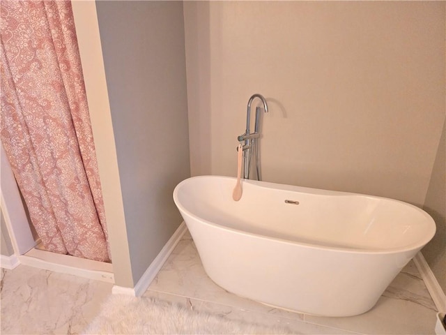 bathroom with marble finish floor, a soaking tub, and baseboards