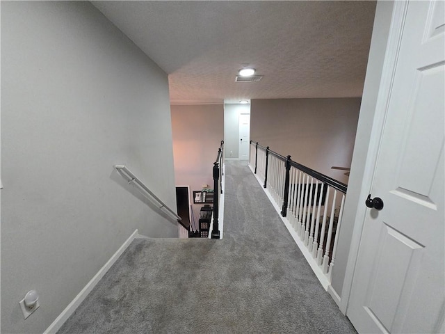 hall with baseboards, dark colored carpet, a textured ceiling, and an upstairs landing