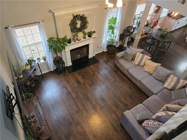 living area featuring a fireplace with raised hearth, dark wood finished floors, visible vents, and baseboards