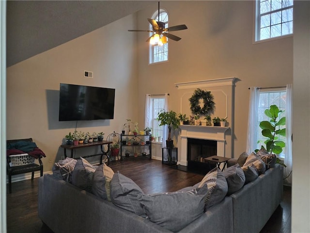 living area with dark wood-style flooring, a fireplace, a towering ceiling, and ceiling fan