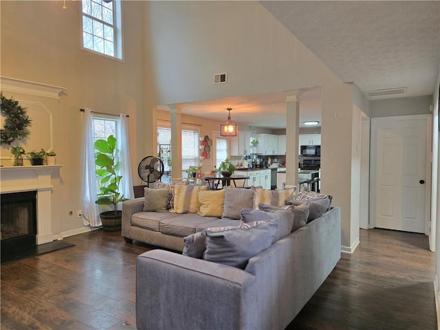 living room with dark wood-style floors, a fireplace with raised hearth, decorative columns, and visible vents