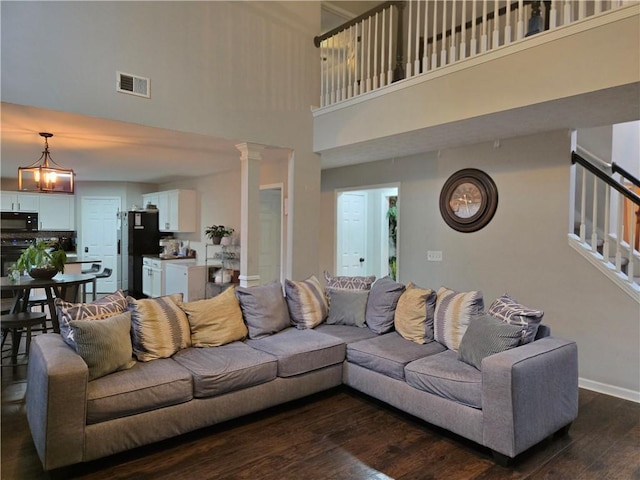 living area featuring visible vents, baseboards, stairway, dark wood-type flooring, and ornate columns