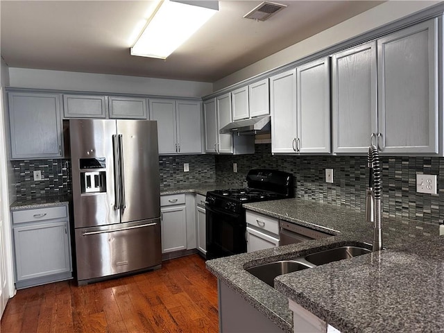 kitchen with black gas range oven, visible vents, dark wood-type flooring, under cabinet range hood, and stainless steel refrigerator with ice dispenser