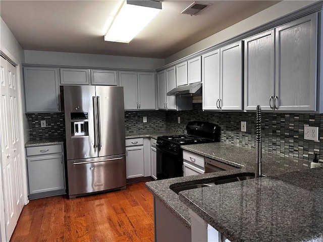 kitchen with visible vents, under cabinet range hood, dark stone counters, stainless steel refrigerator with ice dispenser, and black range with gas cooktop