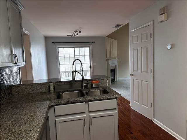 kitchen featuring a sink, dark stone countertops, a peninsula, a glass covered fireplace, and dark wood-style flooring