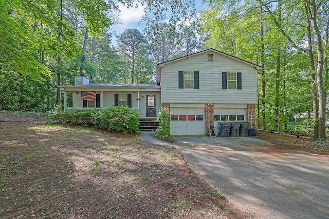 tri-level home featuring a garage, a chimney, brick siding, a porch, and driveway