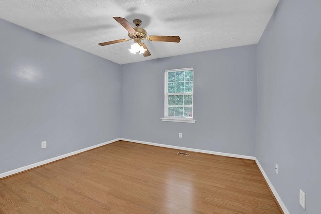 empty room with a textured ceiling, a ceiling fan, baseboards, wood finished floors, and visible vents