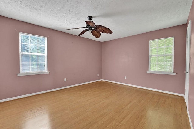 empty room featuring baseboards, a ceiling fan, light wood finished floors, and a wealth of natural light