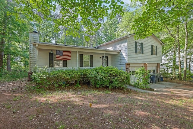 tri-level home with a porch, driveway, a chimney, brick siding, and an attached garage