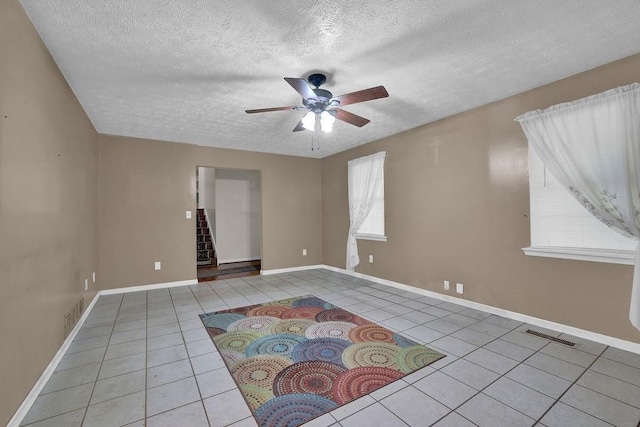 empty room with a textured ceiling, tile patterned floors, visible vents, and a ceiling fan