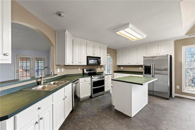 kitchen with appliances with stainless steel finishes, dark tile patterned floors, sink, white cabinets, and a center island