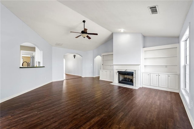 unfurnished living room featuring lofted ceiling, built in shelves, ceiling fan, a premium fireplace, and wood-type flooring