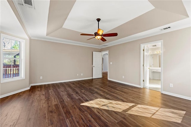 unfurnished bedroom with connected bathroom, ceiling fan, a raised ceiling, dark hardwood / wood-style floors, and crown molding