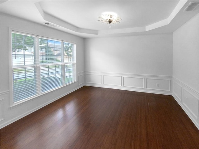 empty room with dark wood-type flooring, a raised ceiling, and an inviting chandelier