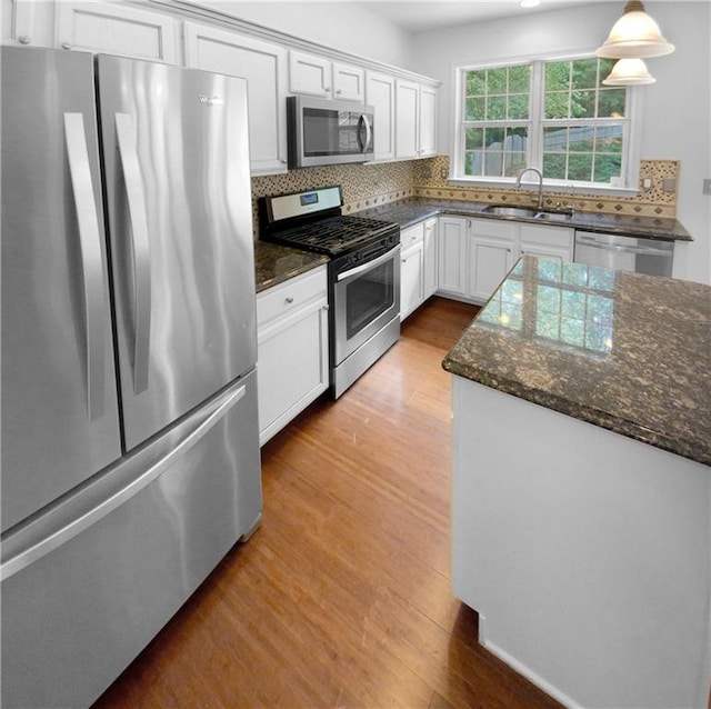 kitchen with light hardwood / wood-style floors, stainless steel appliances, sink, decorative backsplash, and dark stone counters