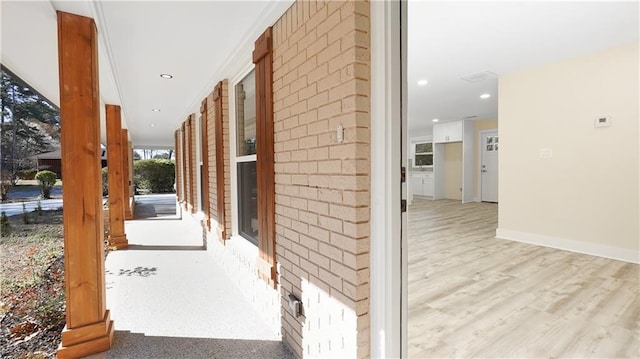 hallway featuring recessed lighting, wood finished floors, baseboards, and brick wall