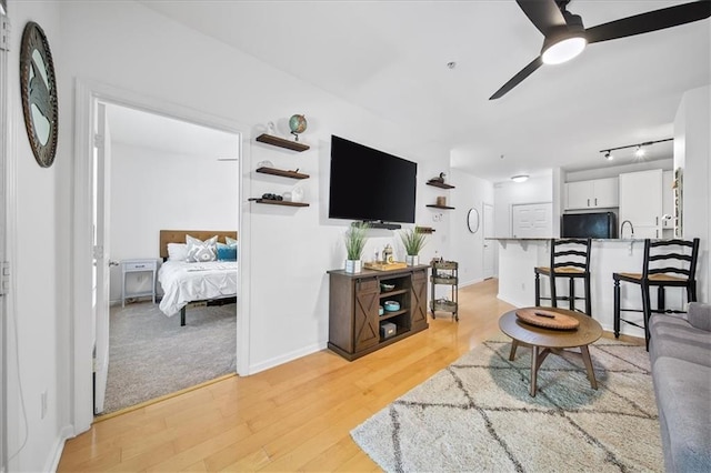 living area featuring light wood-style floors, baseboards, and a ceiling fan