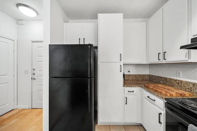 kitchen with light wood-style flooring, under cabinet range hood, white cabinets, freestanding refrigerator, and decorative backsplash