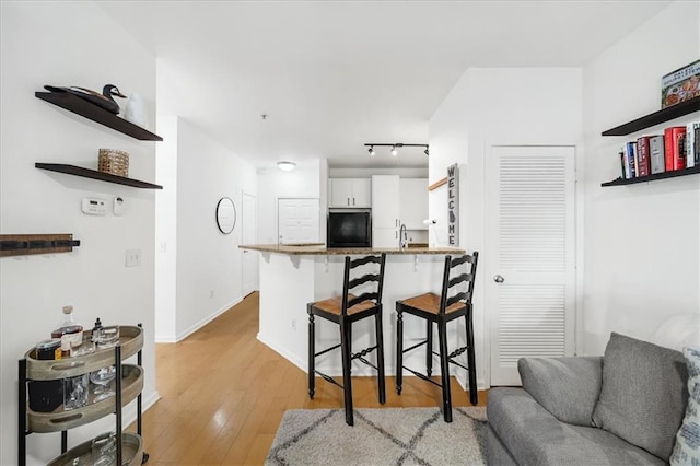 kitchen featuring a breakfast bar, white cabinetry, light wood-type flooring, black refrigerator, and a peninsula