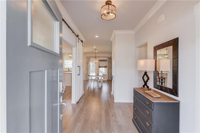 corridor featuring crown molding, a barn door, light wood-style floors, and a notable chandelier