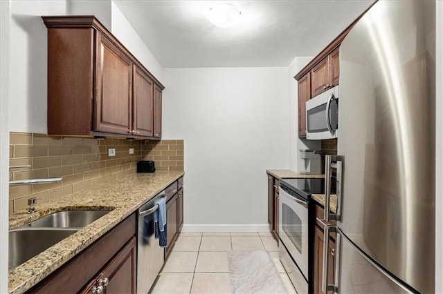 kitchen featuring appliances with stainless steel finishes, tasteful backsplash, light stone counters, sink, and light tile patterned floors