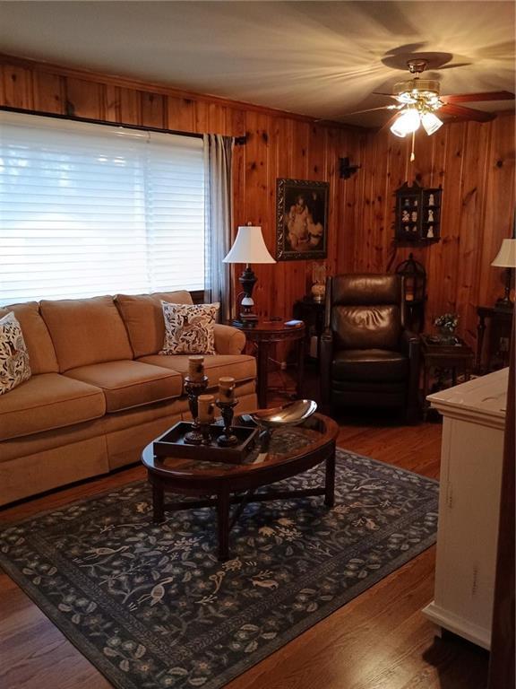 living area with ceiling fan, wooden walls, and wood finished floors