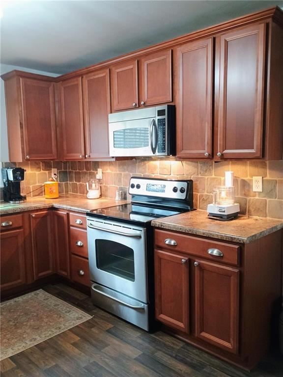 kitchen with brown cabinets, light countertops, decorative backsplash, appliances with stainless steel finishes, and dark wood-type flooring