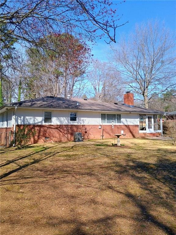 back of house with brick siding, a chimney, and a yard