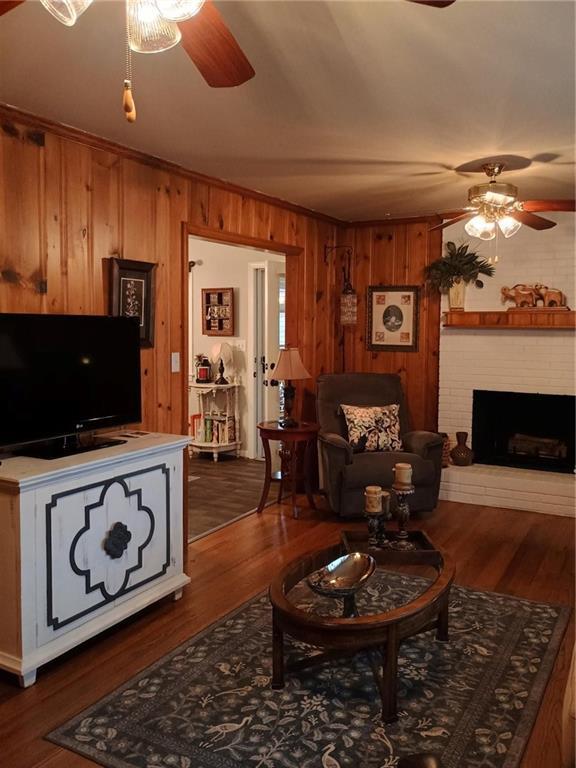 living area featuring a fireplace, ceiling fan, wooden walls, and wood finished floors