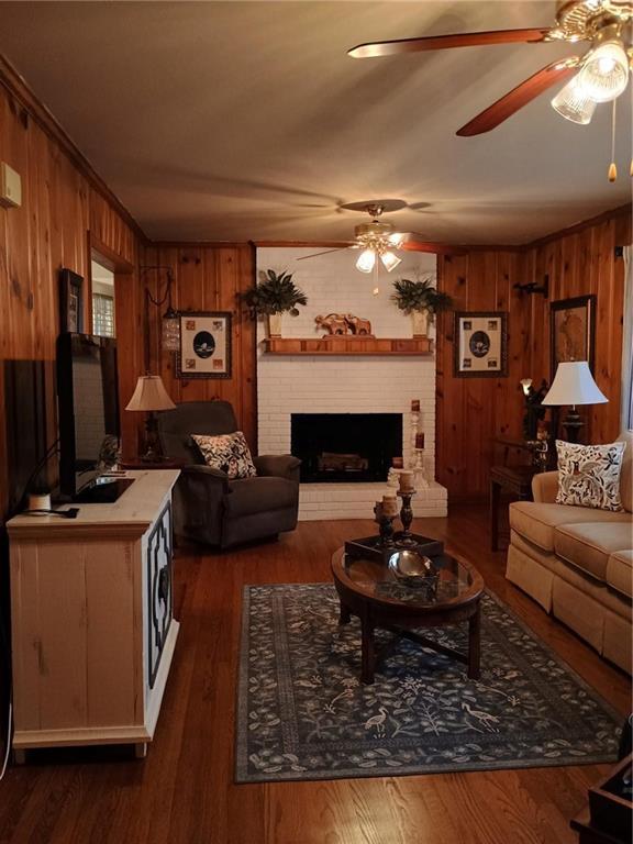 living area with a ceiling fan, a fireplace, wood walls, and wood finished floors