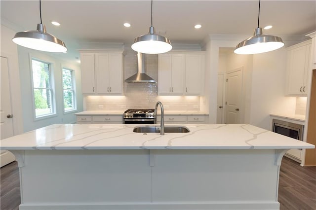 kitchen with pendant lighting, wall chimney range hood, sink, and a center island with sink