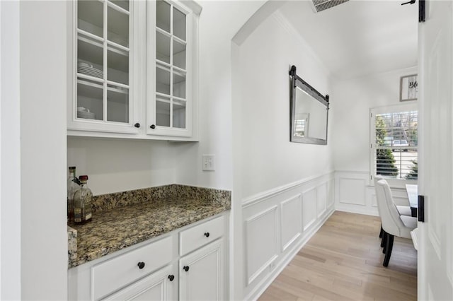 bar featuring dark stone countertops, light hardwood / wood-style floors, a barn door, and white cabinets