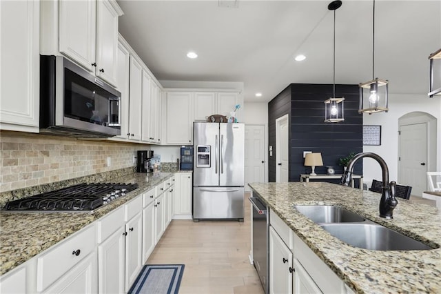 kitchen with sink, appliances with stainless steel finishes, white cabinetry, backsplash, and light stone counters