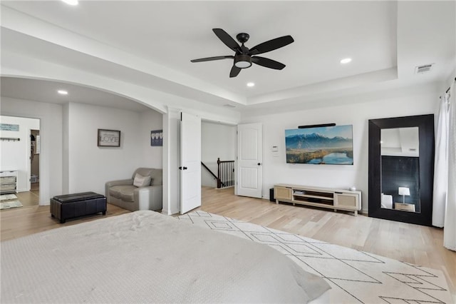 bedroom with ceiling fan, a tray ceiling, and light wood-type flooring