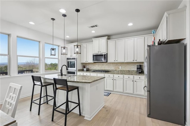 kitchen with appliances with stainless steel finishes, pendant lighting, sink, white cabinets, and a kitchen island with sink