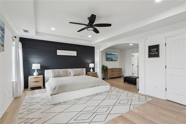 bedroom with a tray ceiling, wood walls, ceiling fan, and light hardwood / wood-style flooring