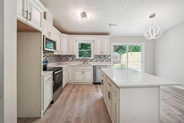 kitchen with light hardwood / wood-style flooring, tasteful backsplash, hanging light fixtures, appliances with stainless steel finishes, and sink