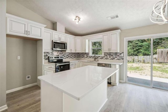 kitchen with appliances with stainless steel finishes, lofted ceiling, light hardwood / wood-style flooring, pendant lighting, and white cabinets