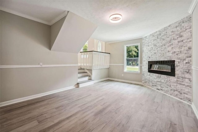 unfurnished living room featuring hardwood / wood-style floors, a stone fireplace, ornamental molding, and a textured ceiling