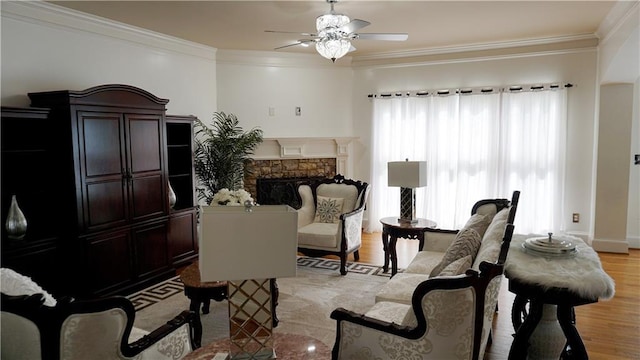 sitting room with crown molding, ceiling fan, light hardwood / wood-style flooring, and a stone fireplace