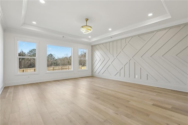 spare room with light wood-type flooring, crown molding, and a raised ceiling