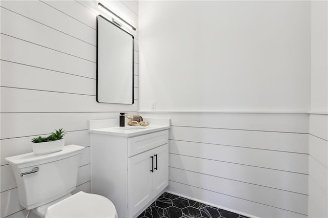 bathroom featuring toilet, vanity, and wood walls