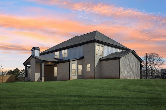 back house at dusk featuring a lawn