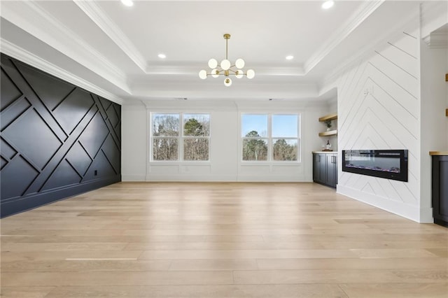 unfurnished living room featuring a large fireplace, crown molding, a tray ceiling, and a notable chandelier