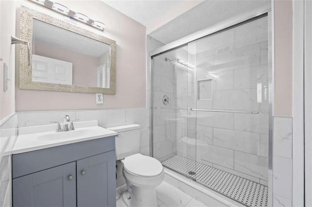 bathroom featuring a shower with shower door, tile walls, vanity, a textured ceiling, and toilet