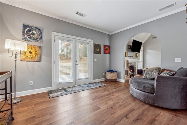 living area with ornamental molding, french doors, wood finished floors, a warm lit fireplace, and baseboards
