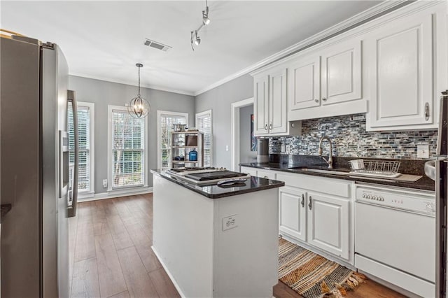 kitchen featuring appliances with stainless steel finishes, dark countertops, a sink, white cabinetry, and a kitchen island