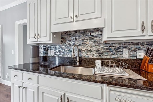 kitchen with a sink, white cabinetry, backsplash, dark stone countertops, and baseboards