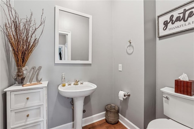 half bathroom with toilet, baseboards, and wood finished floors