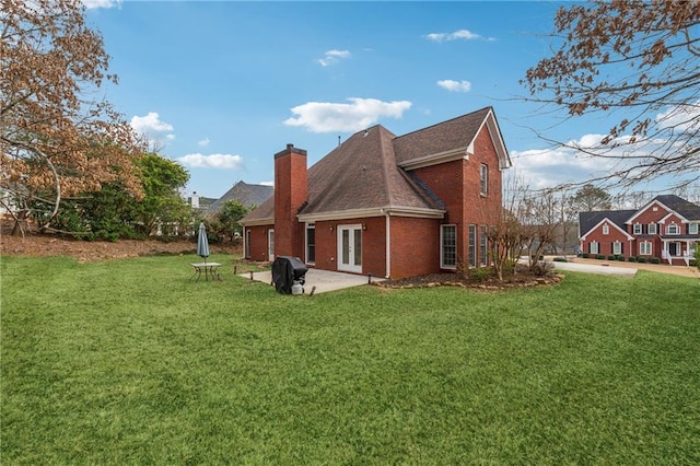 back of property with brick siding, a chimney, a yard, and french doors